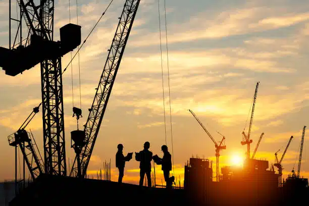 Silhouettes of construction workers shaking hands on a building site, with towering cranes and a sunset in the background, highlighting the construction and civil engineering industry.