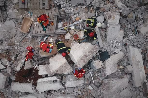 Rescue workers in protective gear collaborating to save victims in a collapsed building during an emergency response operation, with debris scattered around the scene.