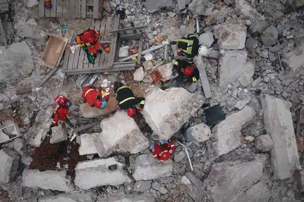Rescue workers in protective gear collaborating to save victims in a collapsed building during an emergency response operation, with debris scattered around the scene.