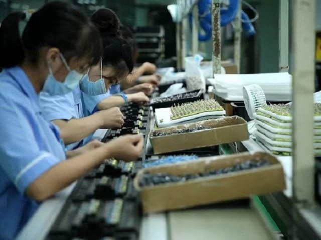 Workers on an assembly line in a factory, carefully assembling electronic components in a well-organized production area, wearing protective gear and focused on quality control.