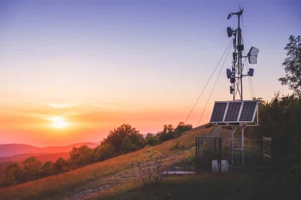 A solar panel and wind turbine setup positioned on a hilltop at sunset, providing off-grid energy for remote operations, with a serene natural landscape in the background.