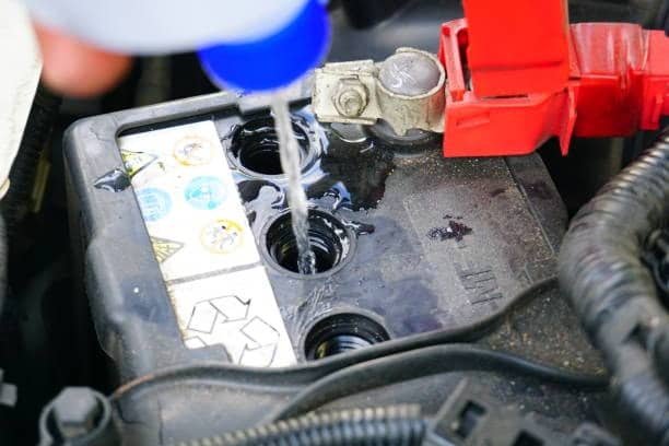 Pouring distilled water into a car battery to maintain proper acid levels