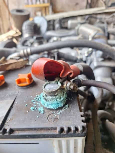 Green corrosion buildup around a car battery terminal indicating acid leakage