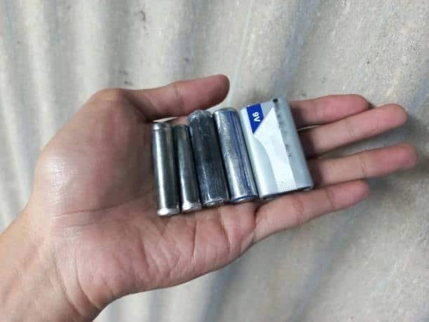 Hand comparing AA batteries with a standard 9V battery