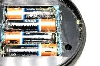 Corroded AA batteries inside a device showing acid leakage and smell risk