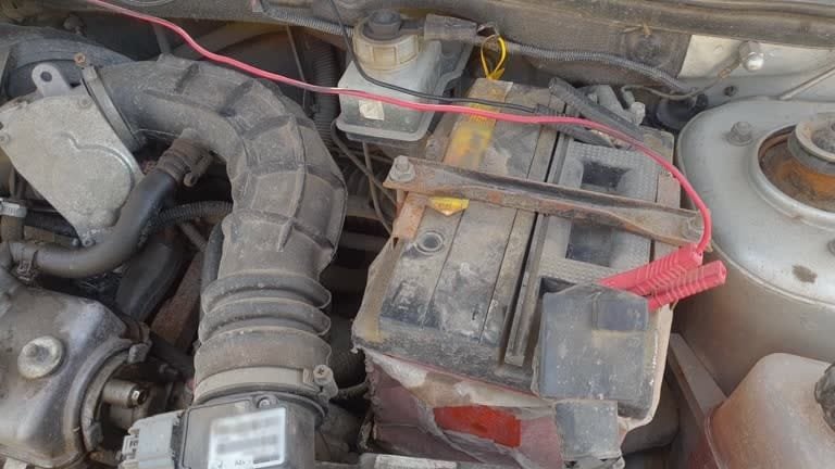 Damaged car battery with acid stains and exposed wiring in engine bay