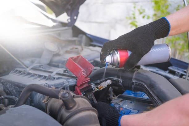 Applying battery cleaner spray to corroded car battery terminals