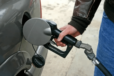 Person pumping gasoline into a car at a fuel station.