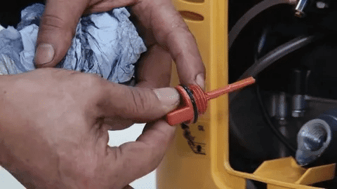 Close-up of hands cleaning generator dipstick before oil change.